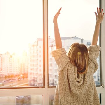 Frau nahe dem Fenster, welches die Hände gegenüberstellt den Sonnenaufgang am Morgen anhebt